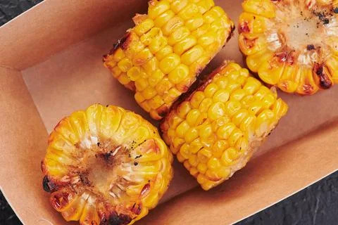 Grilled corn in a craft container on an isolated dark background. Take away Stock Photos