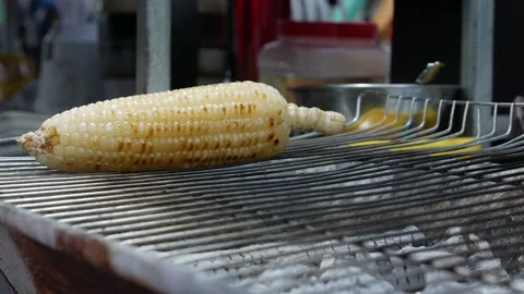 Grilled corn sizzles on an open flame at a bustling night market, its golden Stock Footage 309933477
