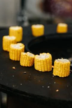 Grilled cut corn cobs on round stove with open fire outdoors, event cooking. Stock Photos