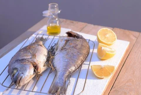 Grilled dorado fish on a grill grate with lemon and olive oil bottle Stock Photos