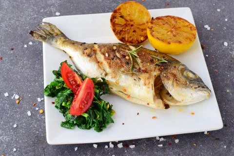 Grilled dorado with grilled lemon, spinach and tomato on a white plate Stock Photos
