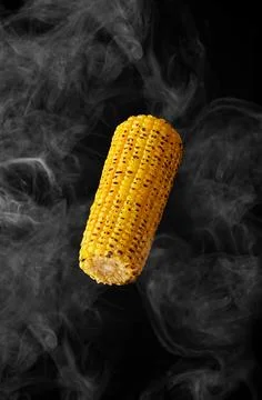 Grilled ear of corn hovering in steam on black background Stock Photos