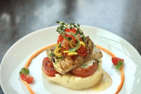Grilled fish with mashed potato and veggies on top served on a white plate Stock Photos
