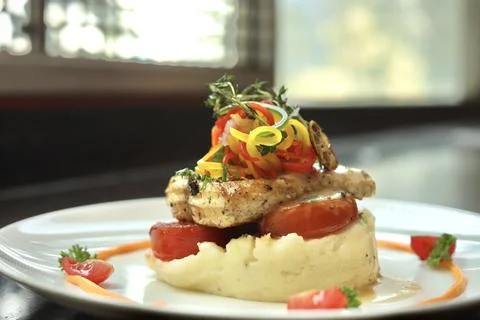 Grilled fish with mashed potato and veggies on top served on a white plate Stock Photos