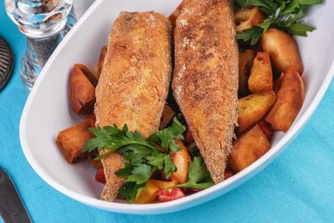 Grilled fish steak is served in batter with braised and roasted potato wedges Stock Photos