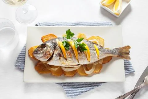 Grilled gilt-head bream with oranges on top of potato slices Stock Photos