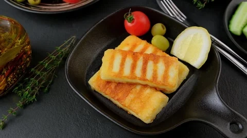 Grilled halloumi cheese in a black pan with olives, tomatoes, cucumbers. Stock Footage 270076834