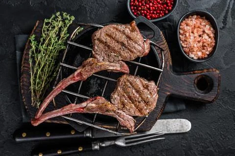 Grilled lamb mutton meat chops steaks on a grill. Black background. Top view Stock Photos