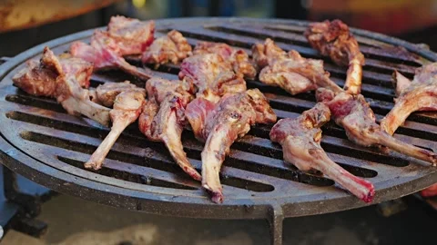 Grilled lamb ribs sizzle on a round metal grill. Some pieces are lightly crisp 動画素材 344631427