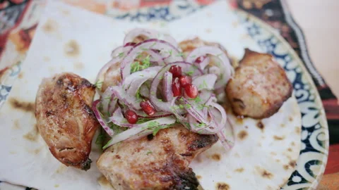Grilled meat pieces served on flatbread topped with onions, herbs, and Stock Footage 332606098
