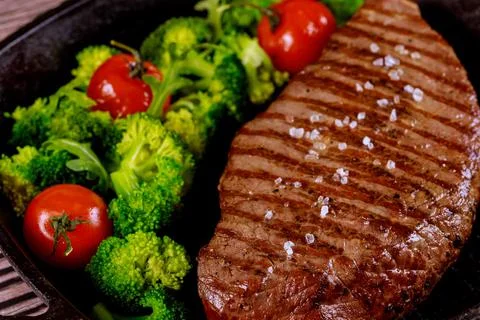 Grilled medium rare beef chop with sea salt, broccoli and tomato on grill pan Stock Photos