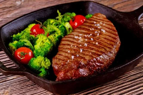 Grilled medium rare beef steak with broccoli and tomato on grill pan. Stock Photos