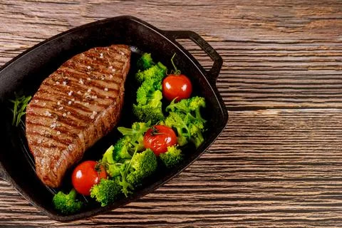 Grilled medium rare beef steak with broccoli and tomato on grill pan. Stock Photos