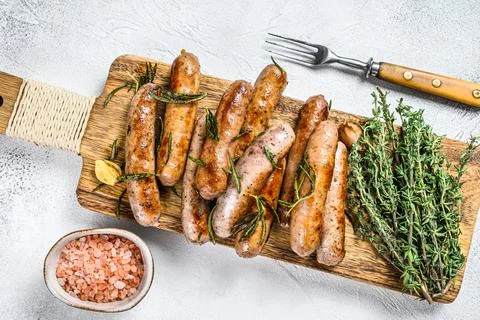 Grilled mix sausages with herbs on a cutting board. White background. Top view Stock Photos