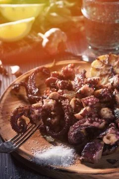 Grilled octopus tentacles on fork on rustic plate close view Stock Photos