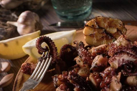 Grilled octopus tentacles on fork on rustic plate macro view Stock Photos