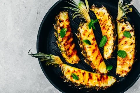 Grilled pineapple with fresh mint in cast iron pan on gray stone background. Stock Photos