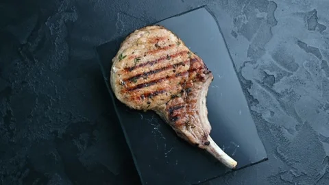 Grilled pork chop prepared with herbs on a black surface Stock Footage 305227655
