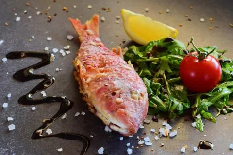 Grilled red mullet on a grey abstract background with rucola salad, balsamic Stock Photos