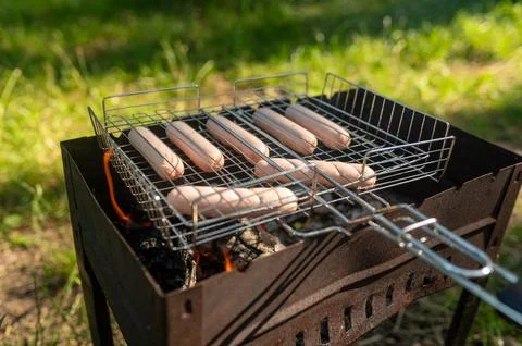 Grilled sausages cooking on open fire during summer picnic Stock Photos