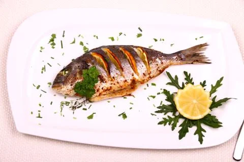 Grilled sea bream fish, lemon, arugula on white plate Stock Photos