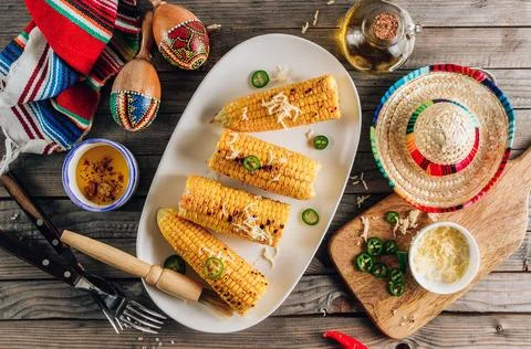 Grilled spicy corn cobs on white plate on rustic wooden background Stock Photos