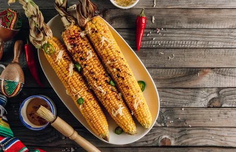 Grilled spicy corn cobs on white plate on rustic wooden background Stock Photos