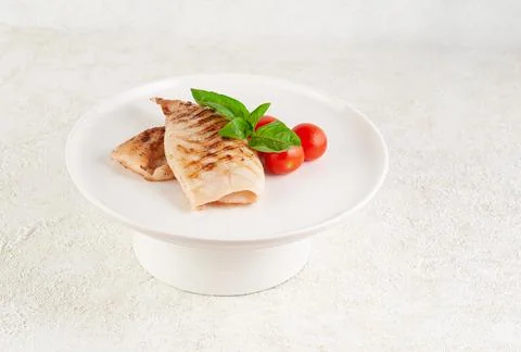 Grilled squid carcass. With cherry tomatoes and basil. On a white plate. Ligh Stock Photos