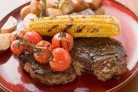 Grilled steak with corn on the cob, cherry tomatoes, potatoes Stock Photos