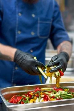 Grilled vegetables in a large container in the kitchen, the cook interferes w Stock Photos