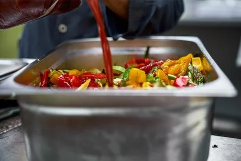Grilled vegetables in a large container in the kitchen, the cook dressing veg Stock Photos