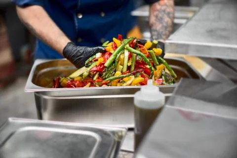 Grilled vegetables in a large container in the kitchen, the cook interferes w Stock Photos