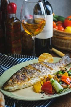 Grilled white fish on a dish on a table in a restaurant with a glass of white Stock Photos
