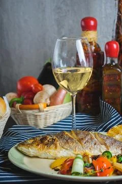 Grilled white fish on a dish on a table in a restaurant with a glass of white Foto stock