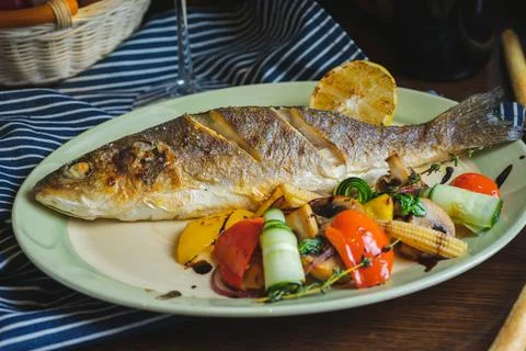 Grilled white fish on a dish on a table in a restaurant with a glass of white Stock Photos