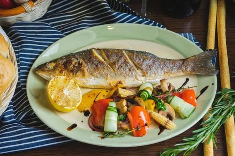 Grilled white fish on a dish on a table in a restaurant with a glass of white Stock Photos