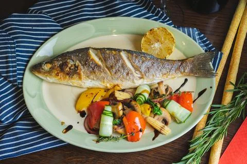 Grilled white fish on a dish on a table in a restaurant with a glass of white Stock Photos