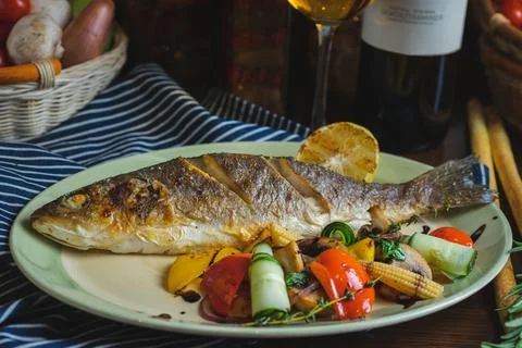 Grilled white fish on a dish on a table in a restaurant with a glass of white Stock Photos