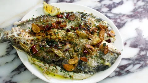 Grilled Whole Fish with Garlic and Herbs Served on Plate Over Marble Tabletop Stock Footage 337651913