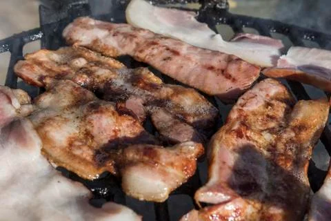 Grilling bacon, pork chop with delicious toasted traces. Smoke. Close up view Stock Photos