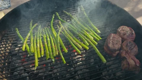 Grilling bacon wrapped beef tenderloin and fresh asparagus on a charcoal BBQ Stock Footage 337435711