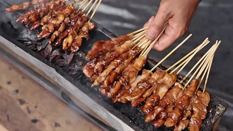 Grilling chicken satay while using a hand fan Stock Footage 273040730