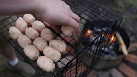 Grilling raw sausages over an open fire, preparing for a delicious outdoor meal Stock Footage 337105196