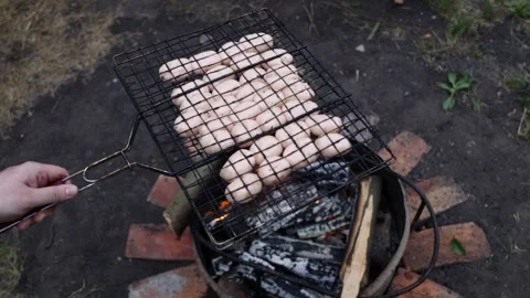 Grilling sausages over an open fire on a barbecue grill outdoors Stock Footage 337105342