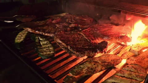 Grilling Steak Over Open Flame Close-up of sizzling steak and vegetables on a Stock Footage 299743154