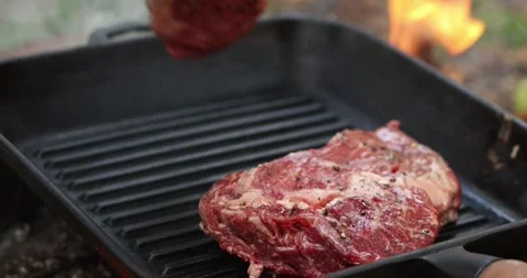 Grilling thick beef steaks on a cast iron pan over open fire Stock Footage 339074051