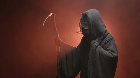 Grim reaper in dark old rags looking at his scythe. Studio portrait on a dark Stock Footage 255829976