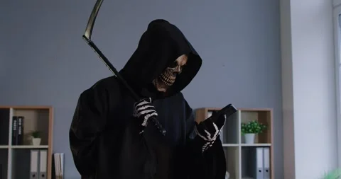 Grim reaper of death in black cloak holding scythe and using smartphone while Stock Footage 313871487