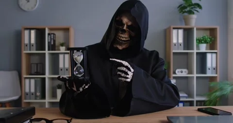 Grim Reaper or Death points to hourglass, emphasizing endless passage of time. Stock Footage 313957574