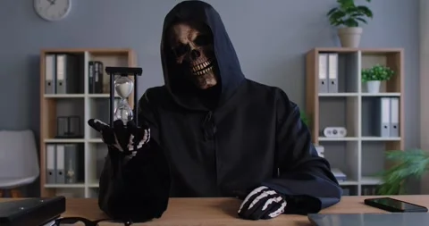 Grim Reaper with sand glass sitting in office workplace reminding of work Stock Footage 314200006
